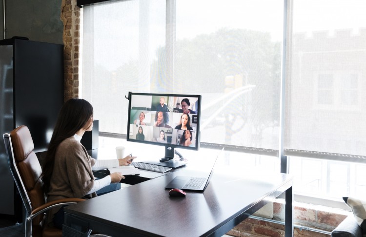 Person sitting at desk in front of a computer.  Large window in the background