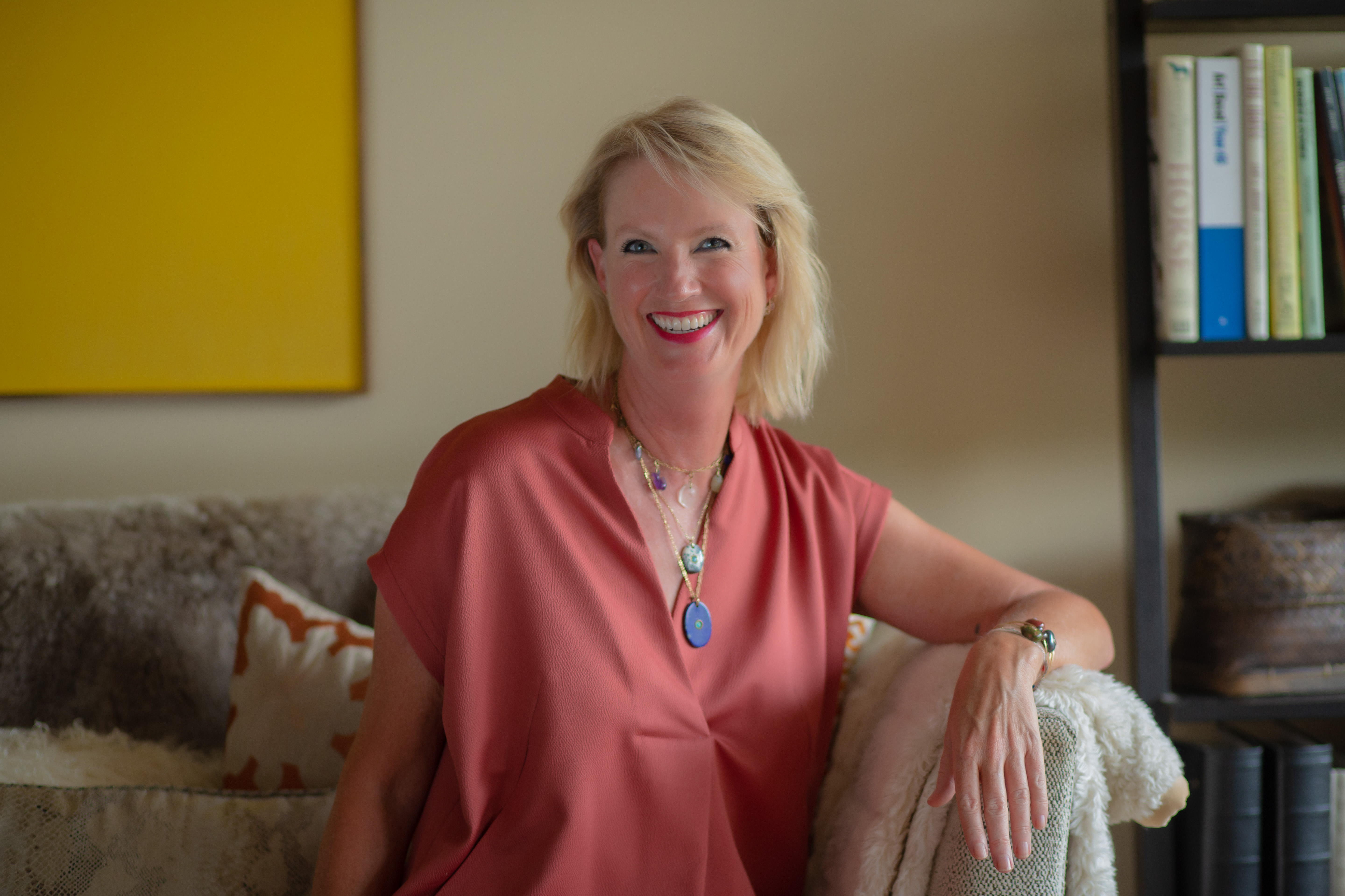 Woman sitting on couch wearing peach shirt. 