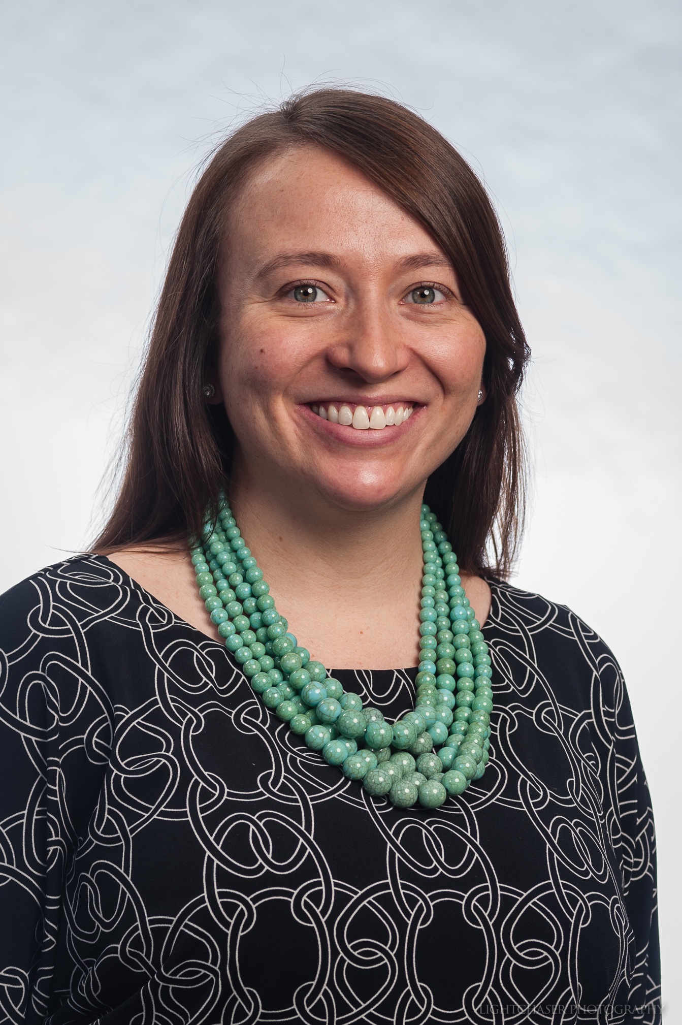 Headshot of Molly, wearing a blue geometric patterned shirt and a green necklace
